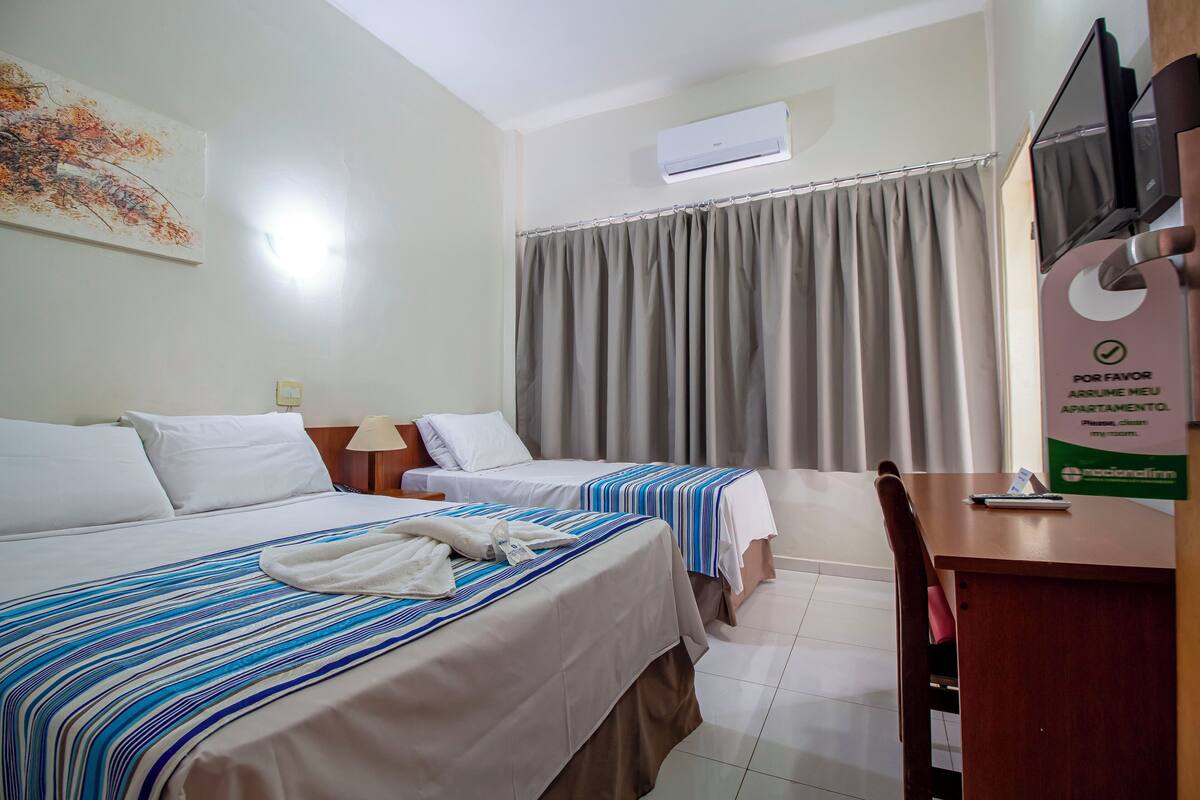 A hotel room with two beds, a desk, a chair, a television, and a window with curtains.