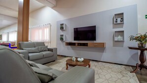 A modern living room with a large flat-screen TV, grey sofas, a coffee table, and decorative shelves. - Hotel Dan Inn Barretos By Nacional Inn  (Barretos)