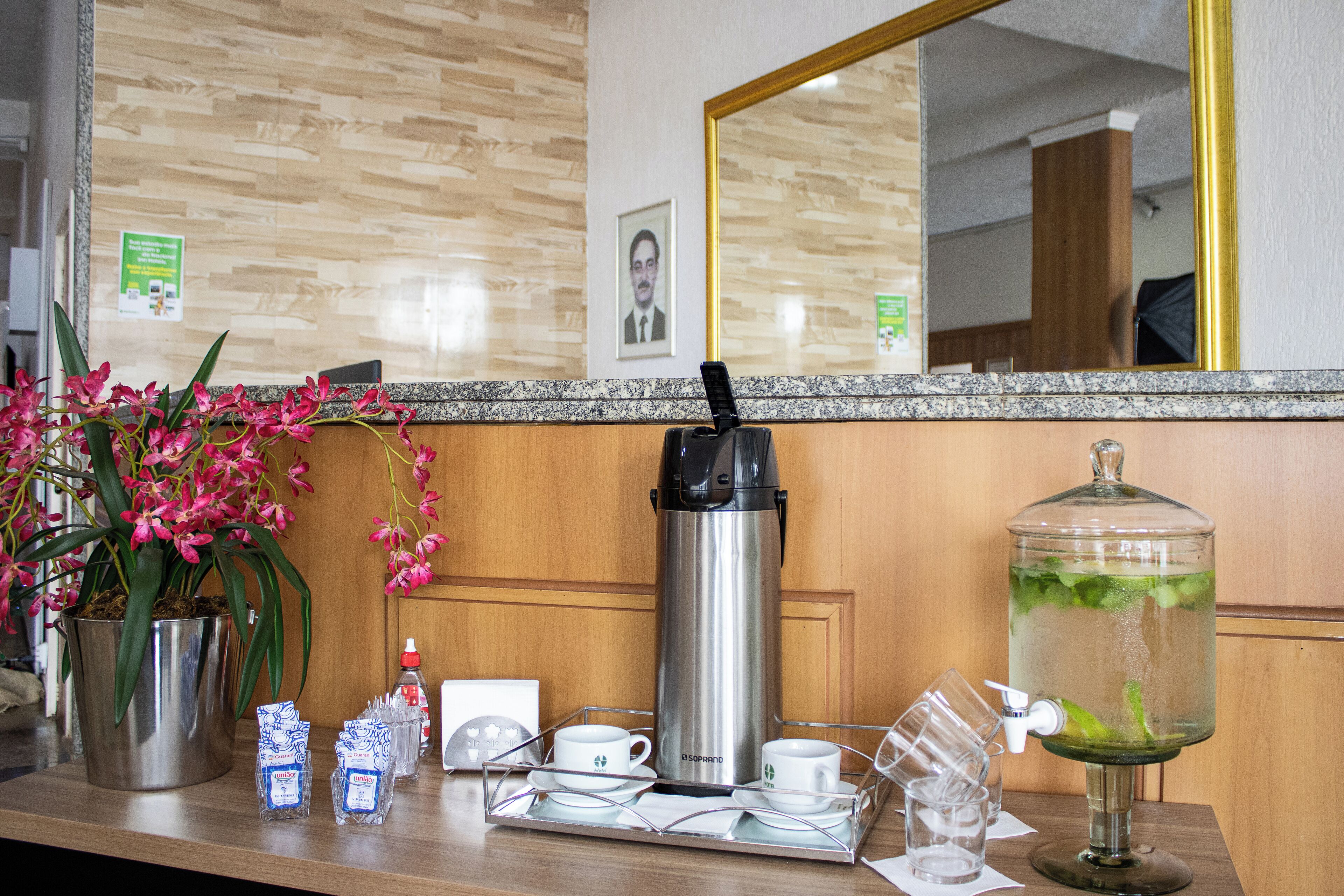 Zona de recepción de un hotel con cafetera, dispensador de agua y una bandeja con tazas y platillos.