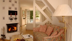 A cozy room with a fireplace, a floral sofa, and a staircase leading to an outdoor area. - Gartenhotel Weisser Hof (Malente)