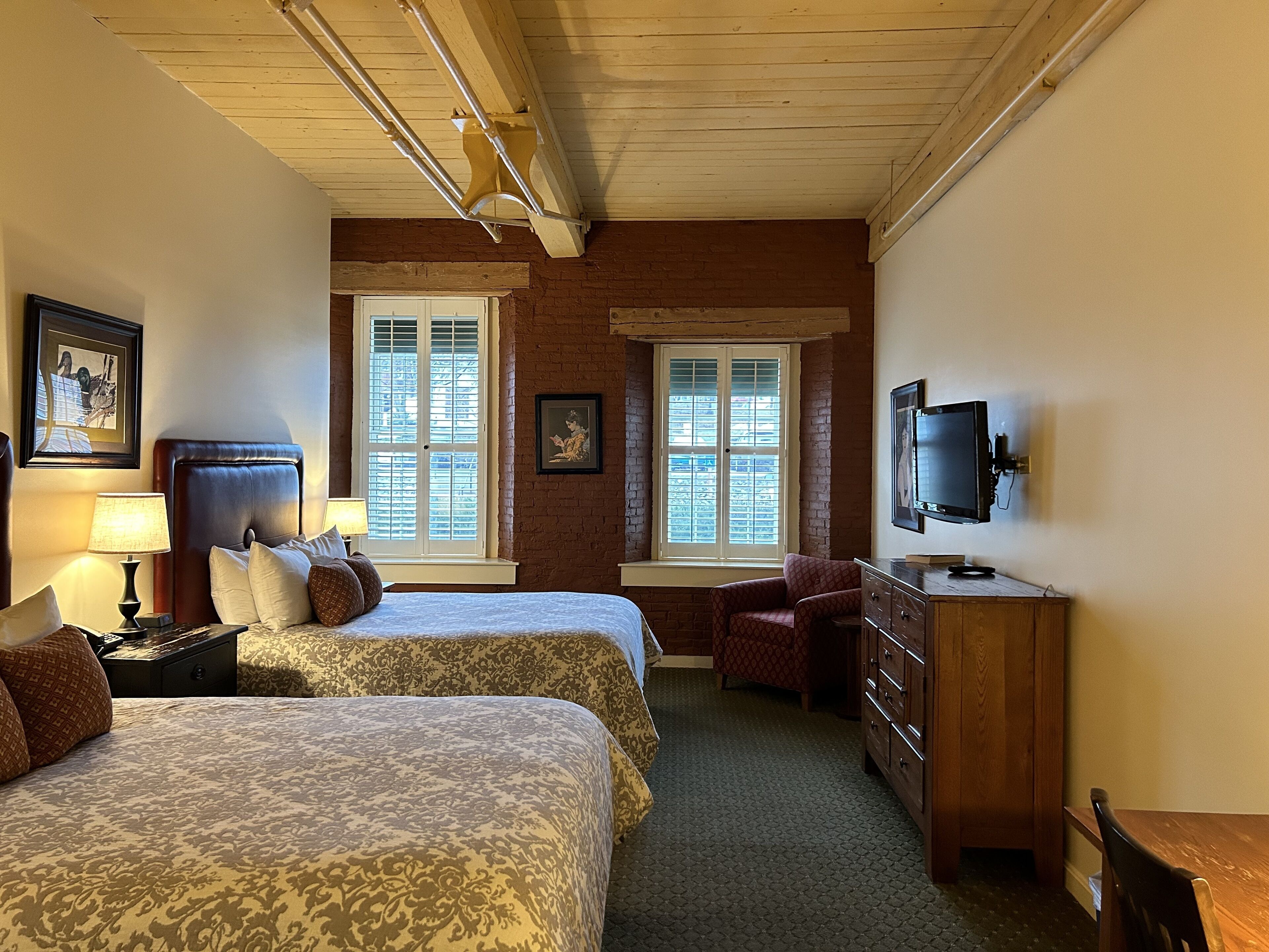 A hotel room with two beds, a TV, a dresser, and a window with blinds.
