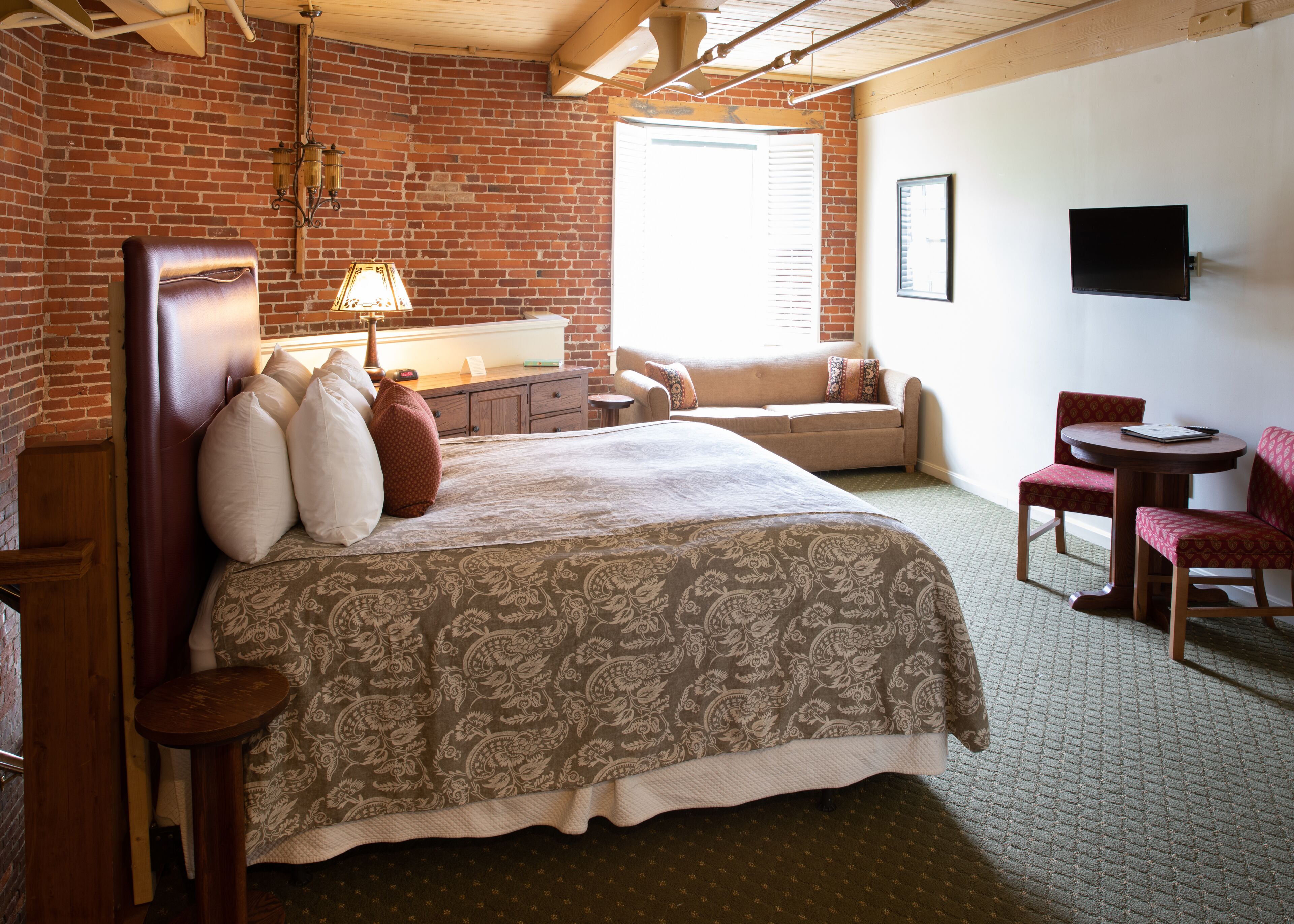 A hotel room with a large bed, a desk, a chair, a TV, and a window with blinds.