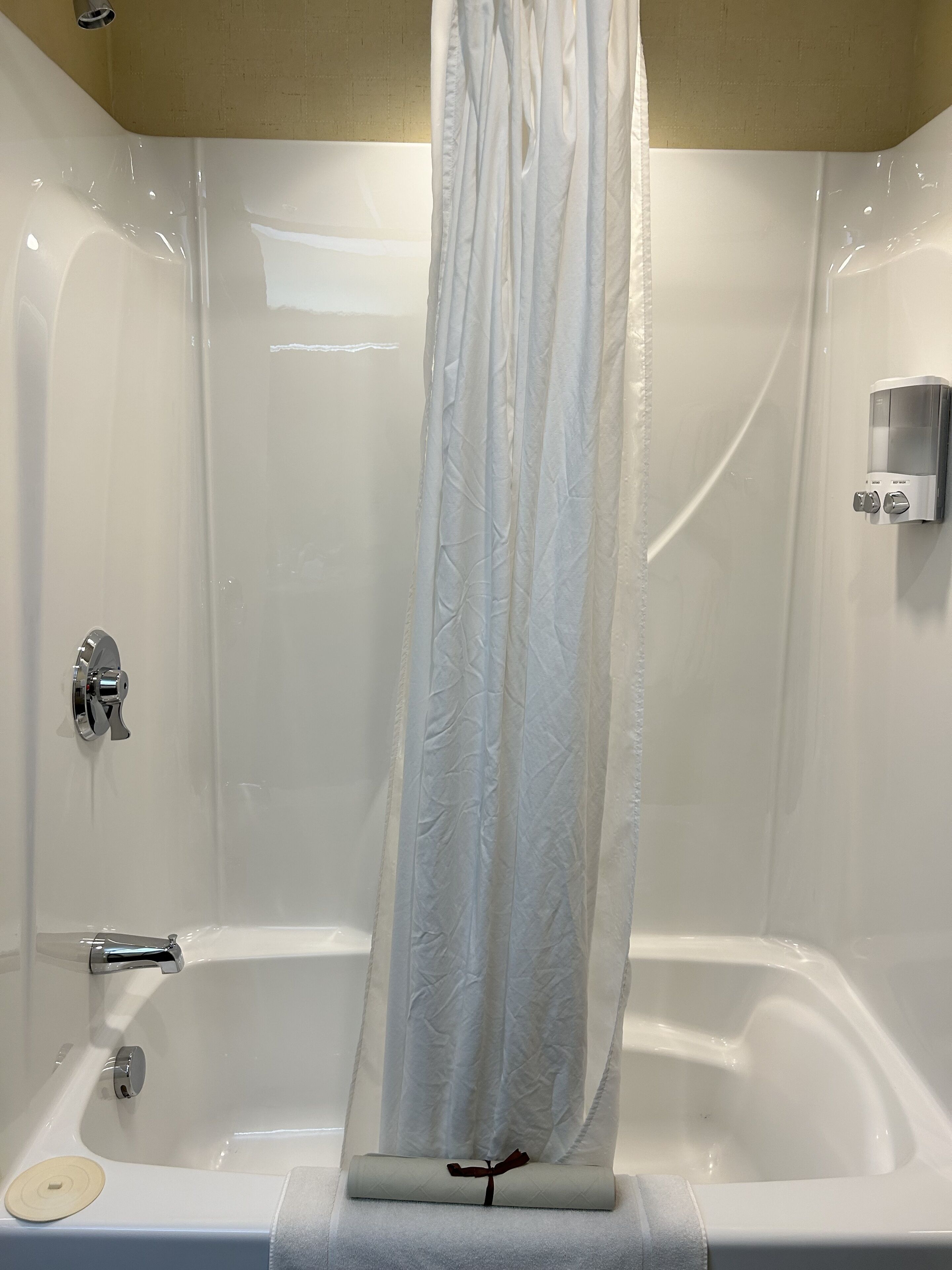 A modern bathroom with a bathtub, a shower curtain, a handheld showerhead, and a soap dispenser.