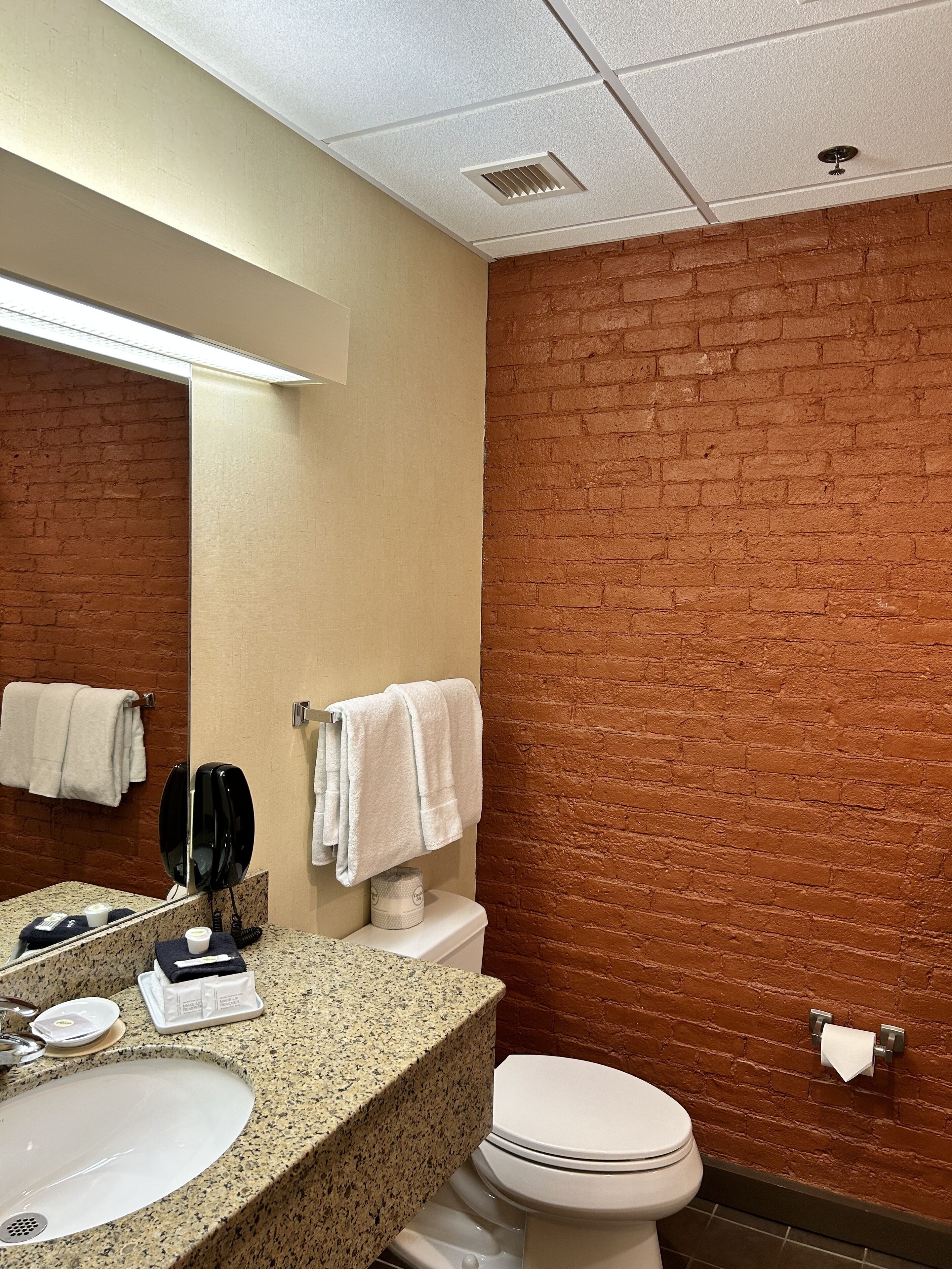 Un baño con lavamanos de encimera de granito, un inodoro blanco y un espejo con teléfono negro.