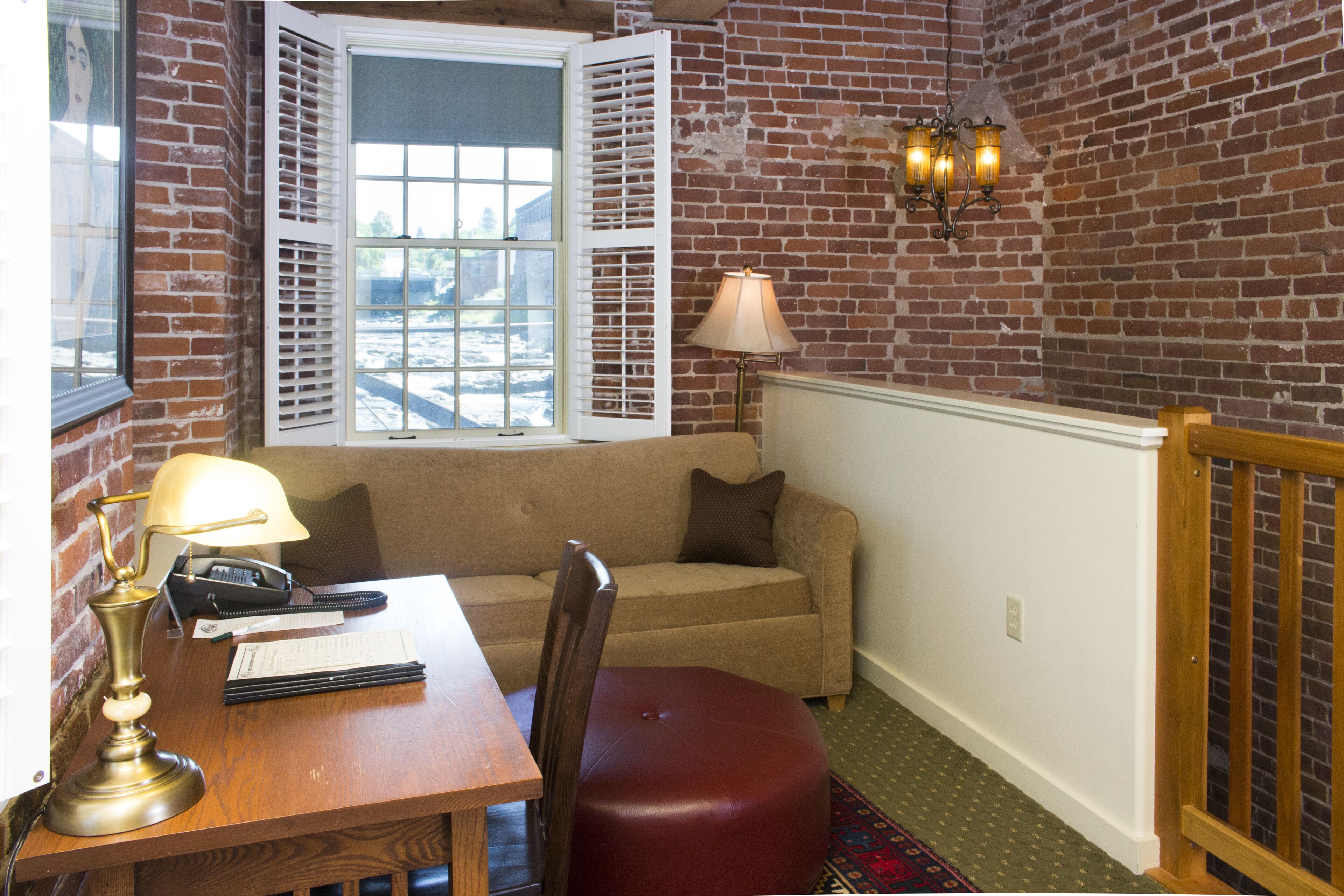 A room with a wooden desk, a leather chair, a sofa, and a window with shutters.