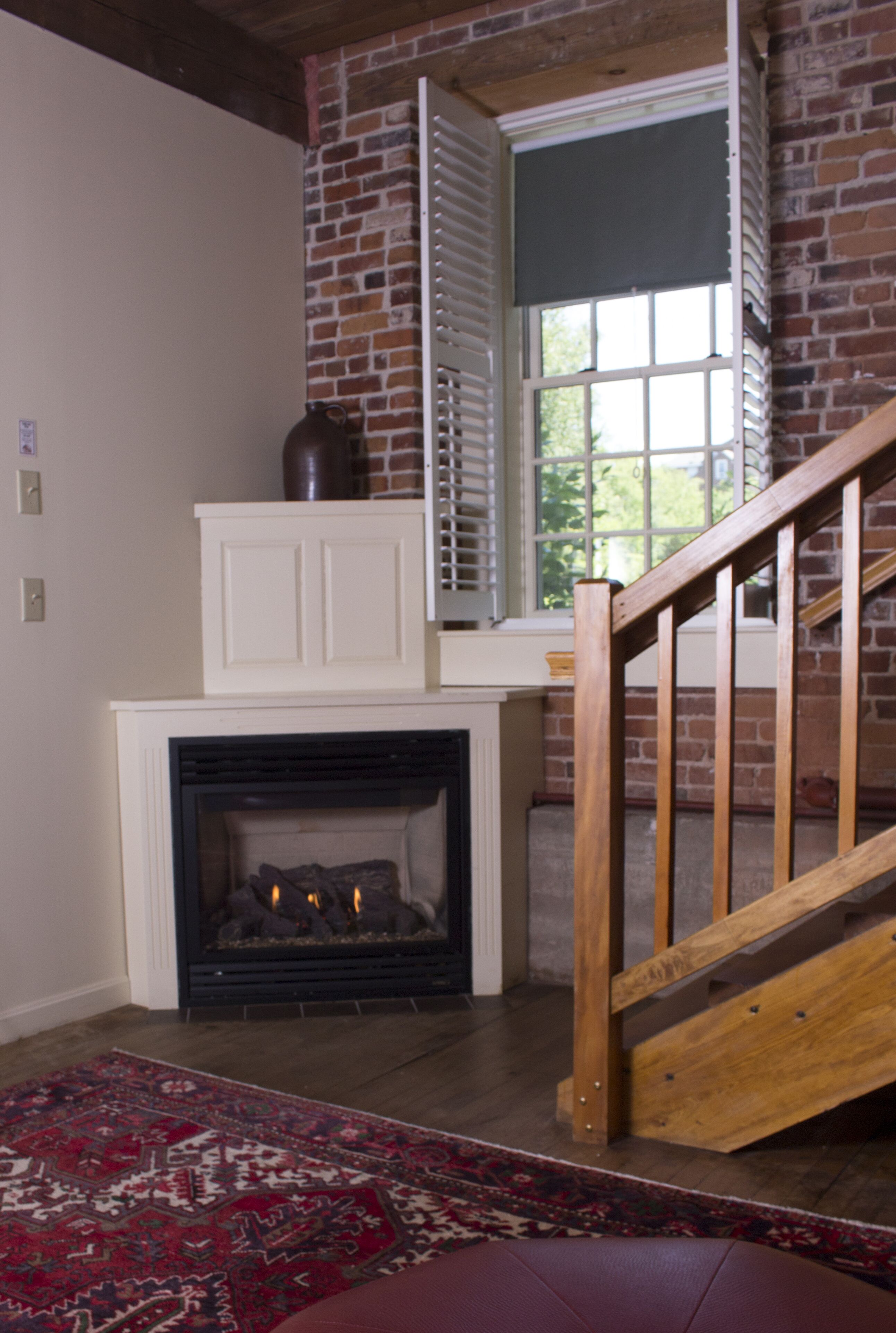 A room with a fireplace, a wooden staircase, and a brick wall.