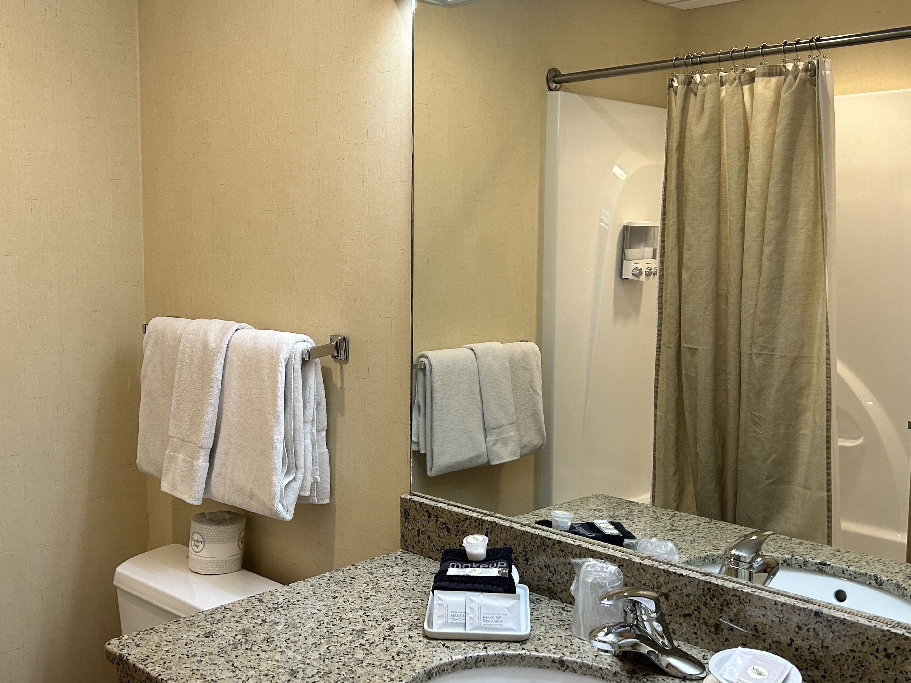 Un baño con encimera de granito, un lavabo, un espejo, un perchero para toallas y una cortina de ducha.