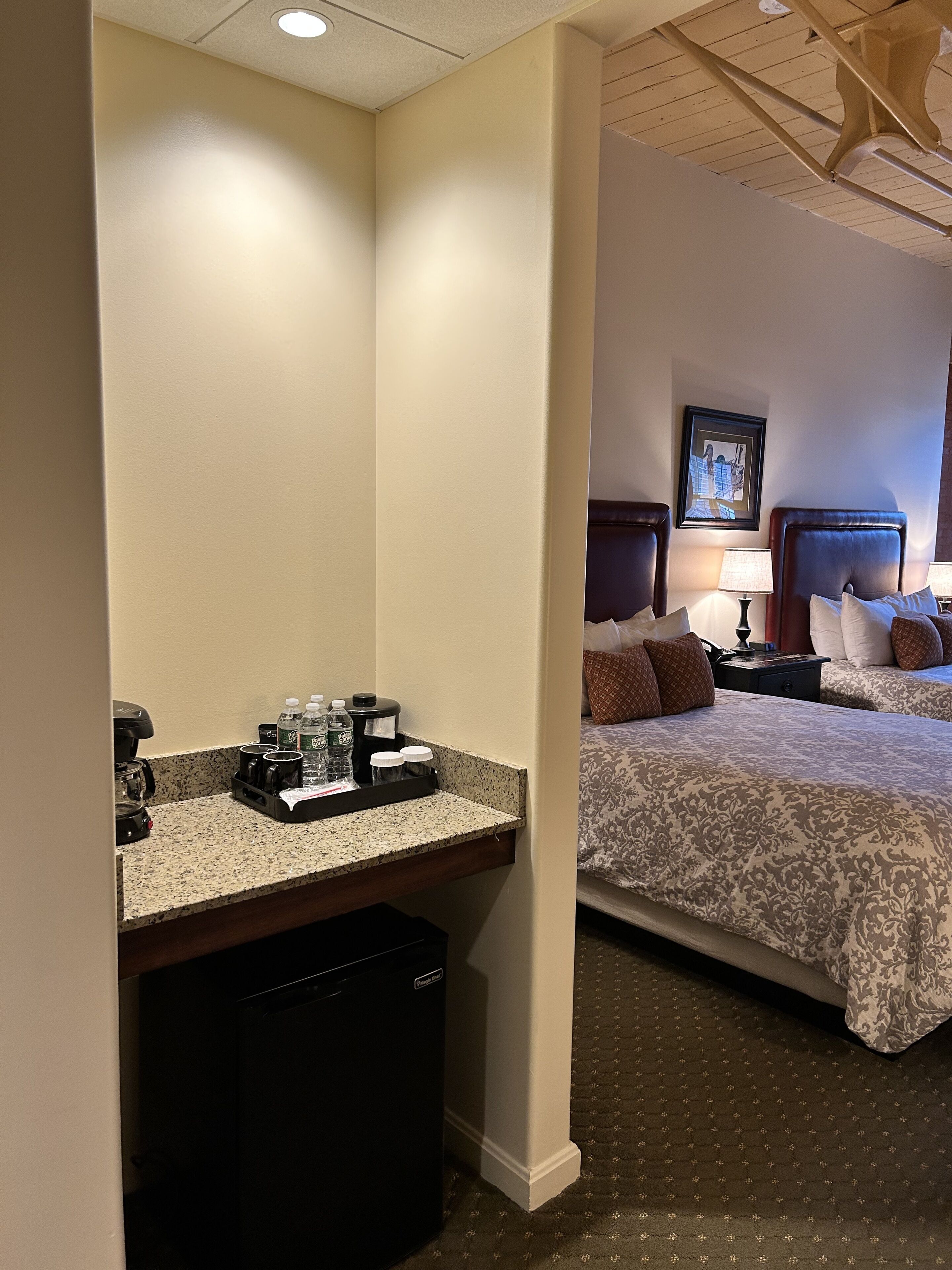 A hotel room with a bed, bedside tables, a coffee station, and a small trash bin.