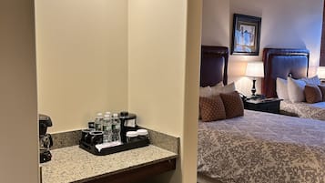 A hotel room with a bed, bedside tables, a coffee station, and a small trash bin.