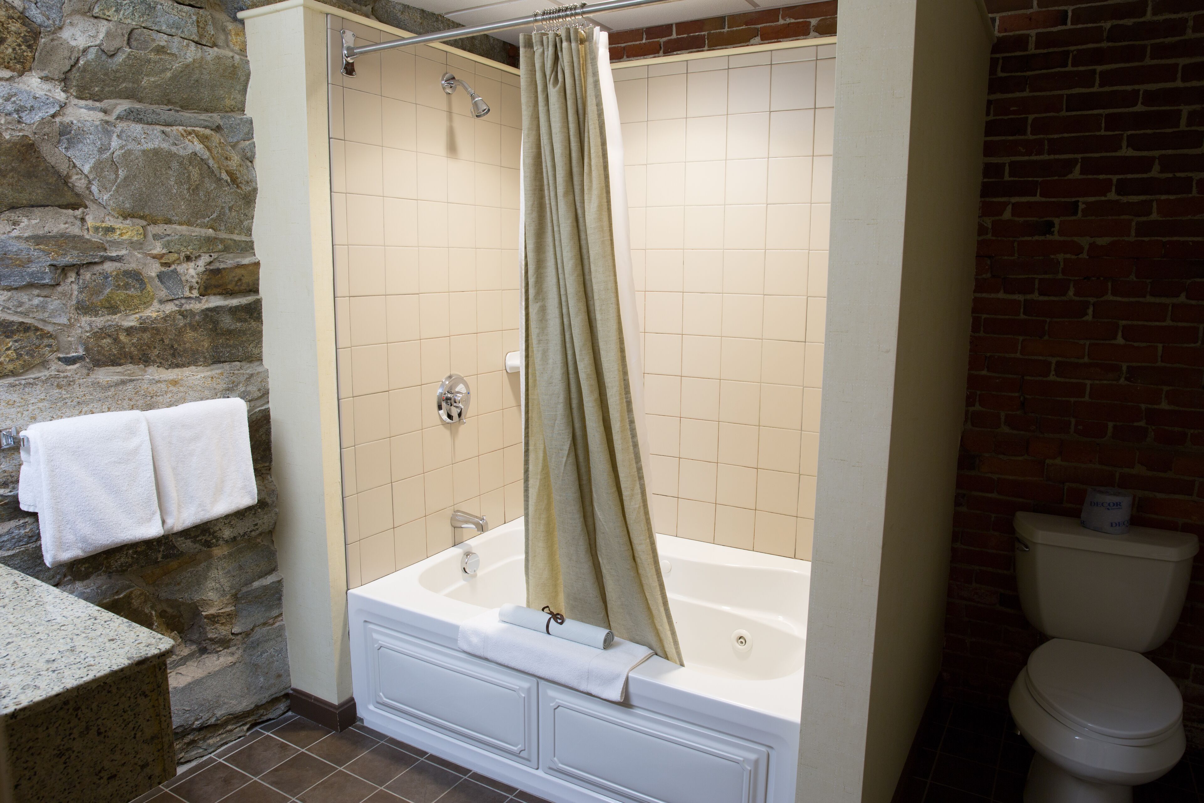 Un baño con pared de piedra, una bañera, un cortinón de ducha, un inodoro y un lavamanos.