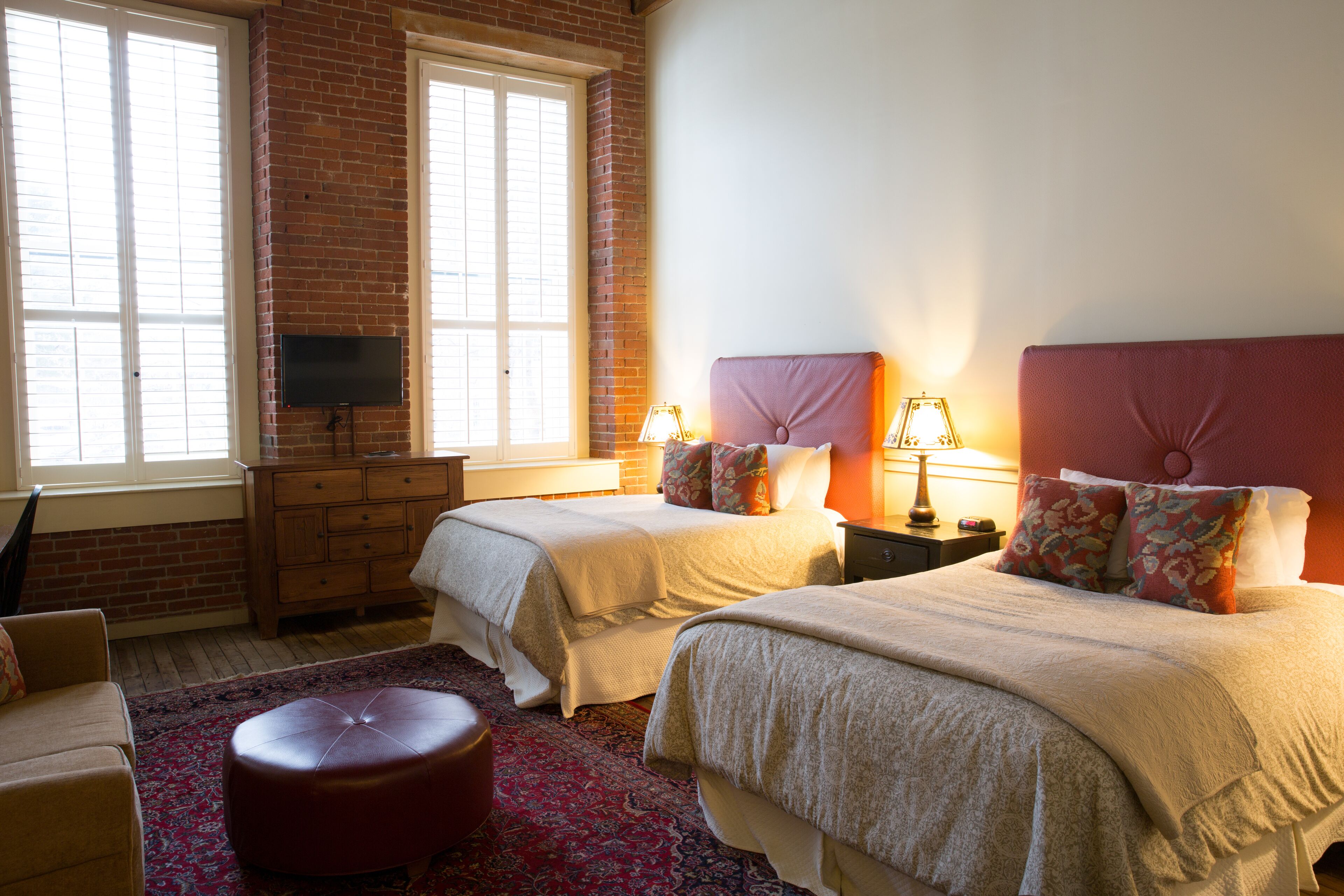 A bedroom with two beds, a television, a dresser, and a red carpet.