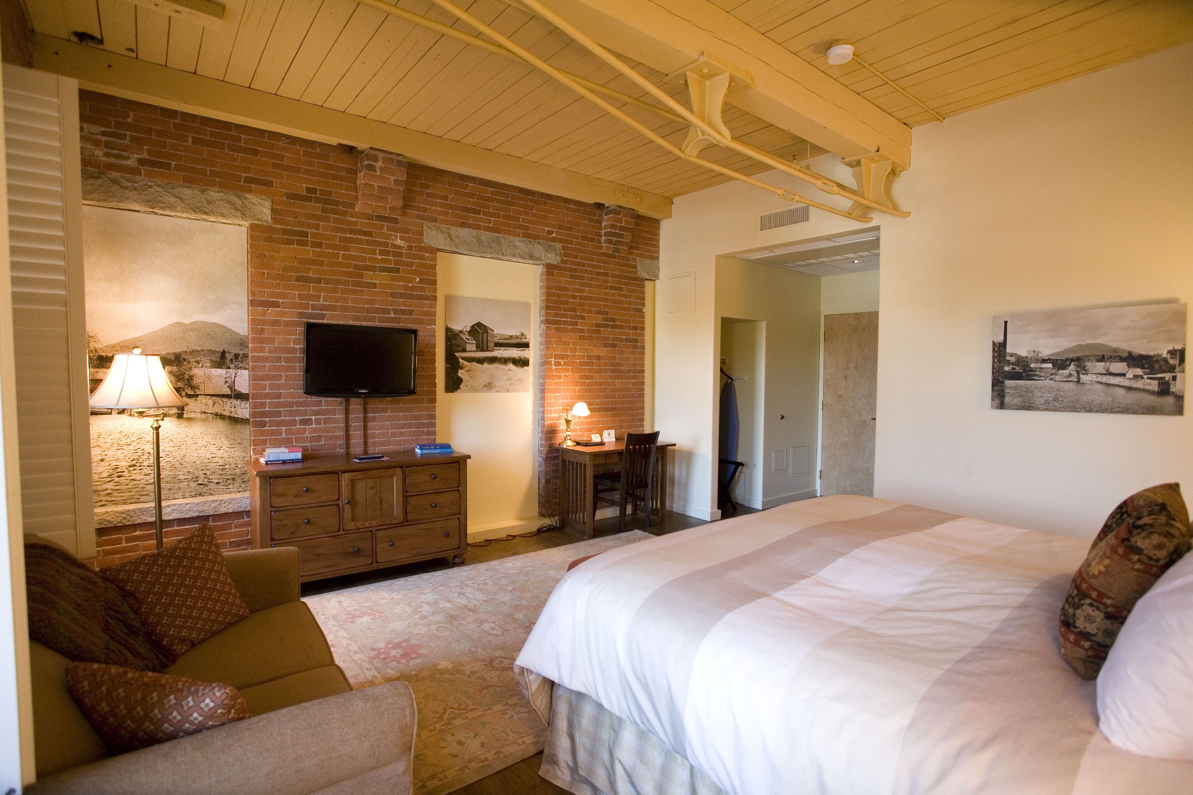 Een slaapkamer met een groot bed, een bureau met stoel, een televisie en een bakstenen muur.