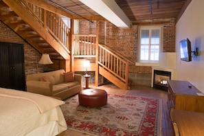 A cozy room with a wooden staircase, a fireplace, a sofa, and a patterned rug.