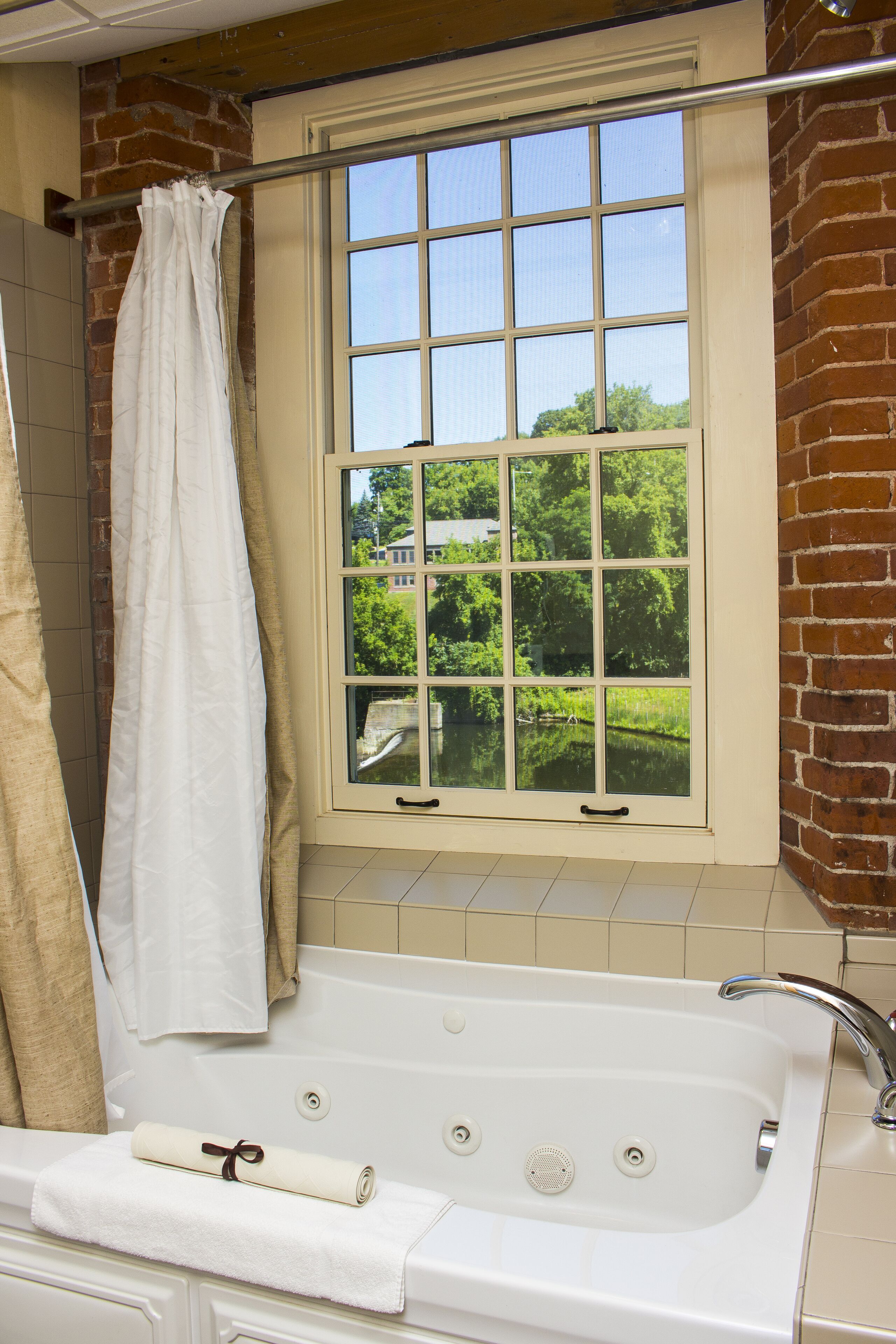 A bathroom with a bathtub, a window with a view of greenery, and a towel on the tub.