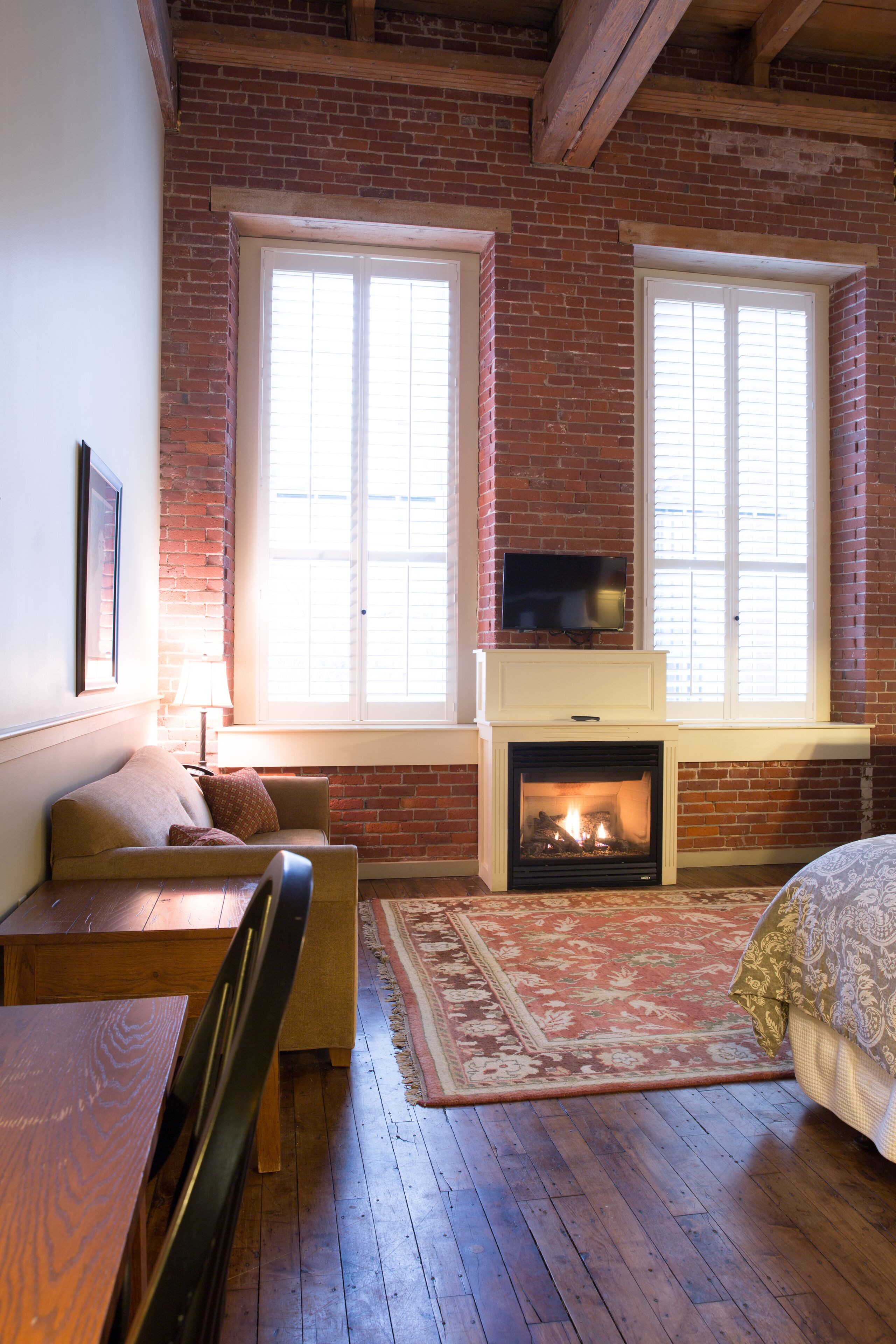 A cozy room with a fireplace, wooden furniture, and large windows.