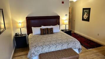 A neatly arranged bedroom with a large bed, bedside lamps, a bench, and a framed picture on the wall.