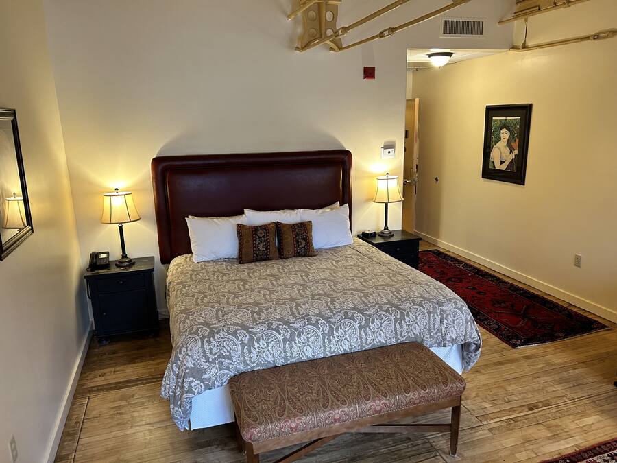 A neatly arranged bedroom with a large bed, bedside lamps, a bench, and a framed picture on the wall.