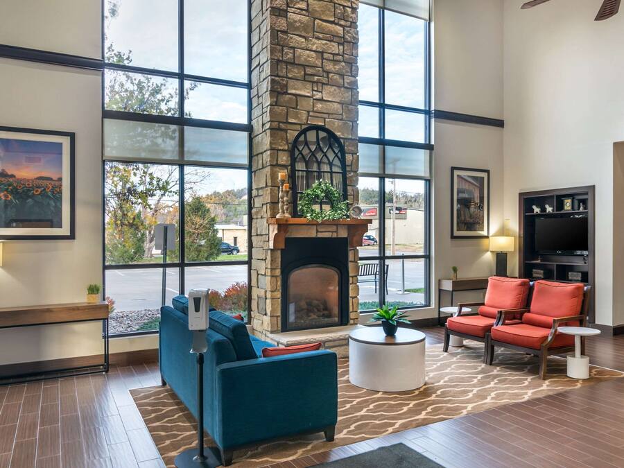A spacious lobby with a stone fireplace, large windows, a blue sofa, and red chairs.
