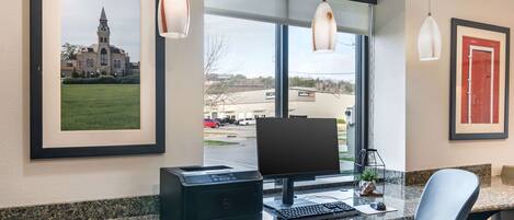 A hotel reception desk with a desktop computer, printer, and a framed picture of a building.