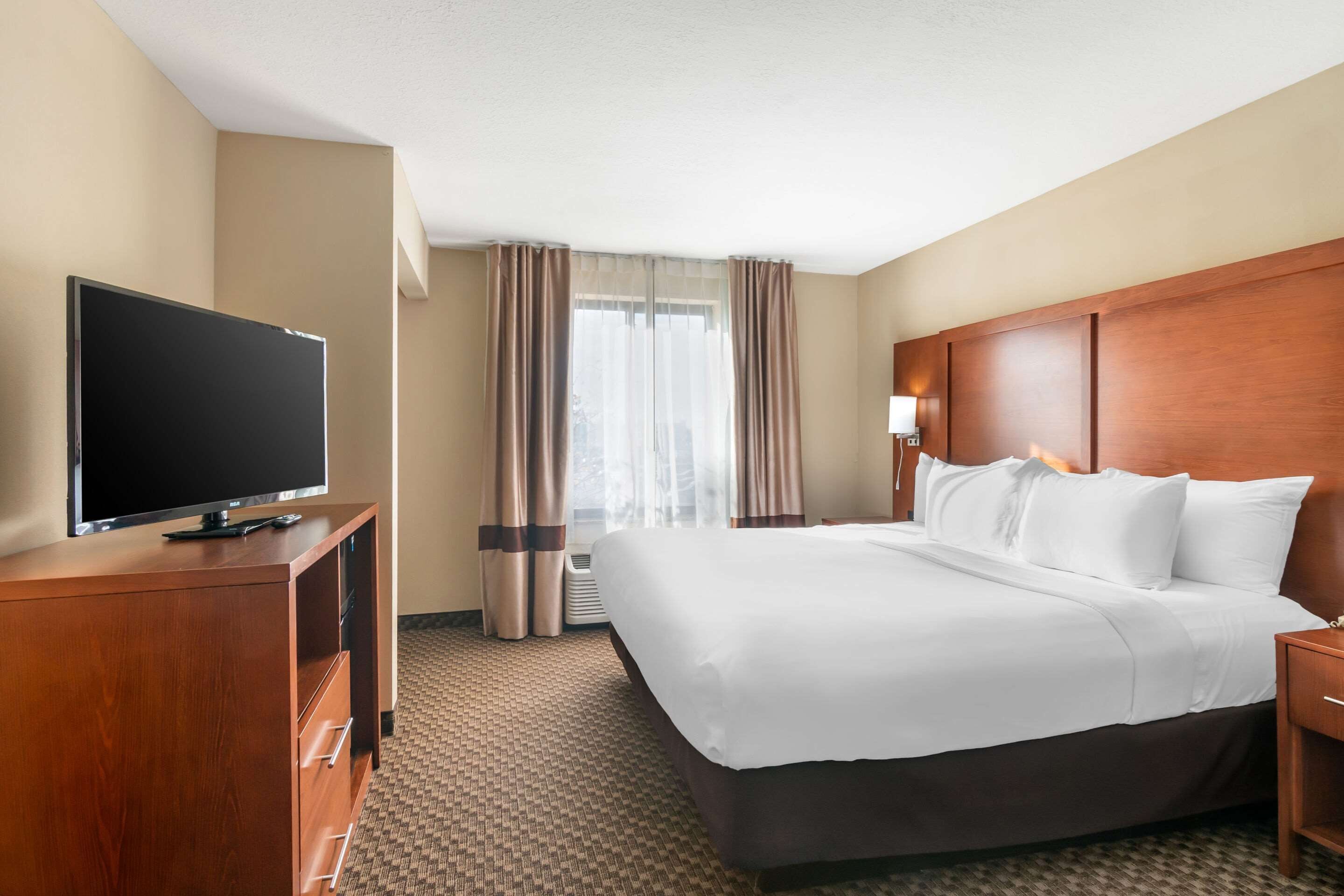 Habitación de hotel con una cama grande, un televisor de pantalla plana sobre una cómoda de madera y una ventana con cortinas.