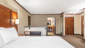 Une chambre d’hôtel avec un grand lit, un bureau avec une chaise, un miroir et une porte donnant sur une salle de bain.