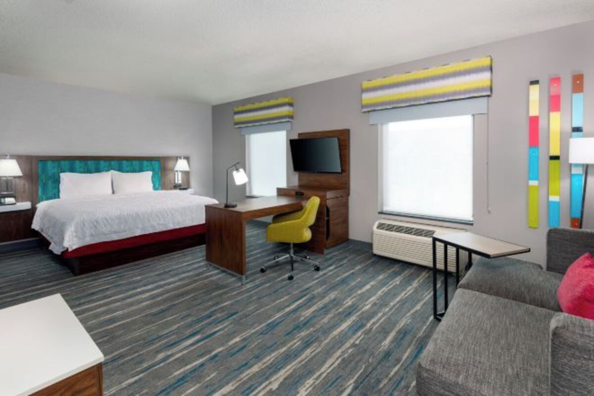 A hotel room with a bed, desk, chair, TV, and a couch.