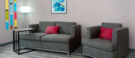 A modern room with a grey sofa and armchair, a small side table, a floor lamp, and a framed picture on the wall.
