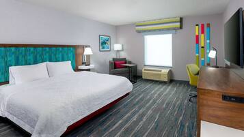 A hotel room with a large bed, a desk, a chair, a window, and a TV.