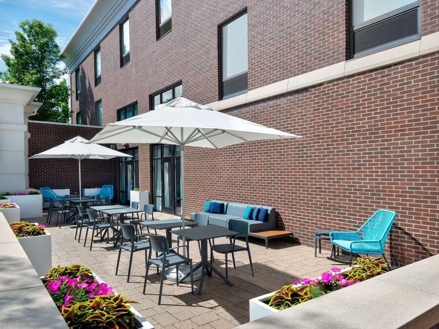 An outdoor patio with tables, chairs, and umbrellas, adjacent to a brick building.