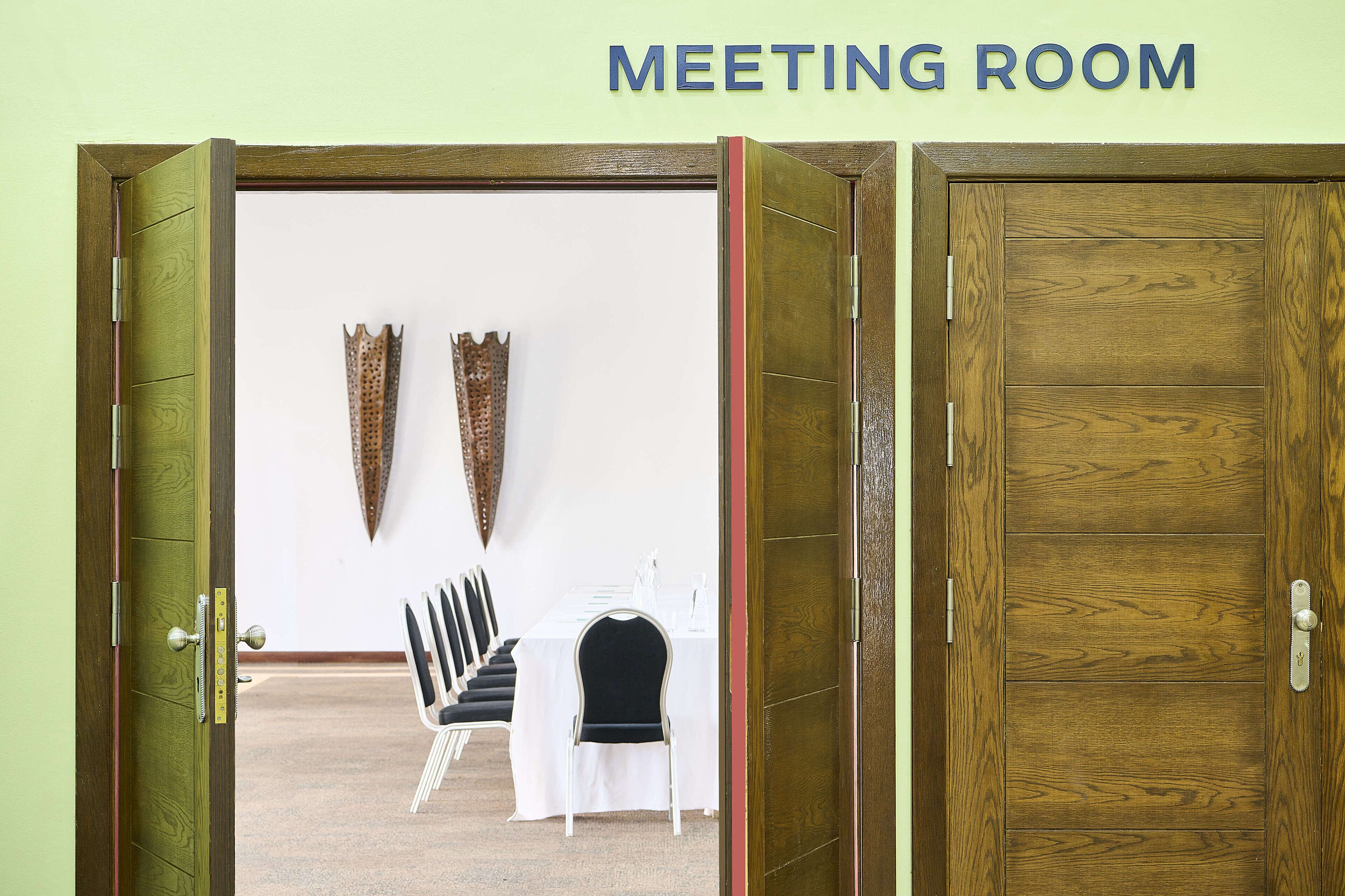 A meeting room with a wooden door, a table with chairs, and two wall-mounted decorations.