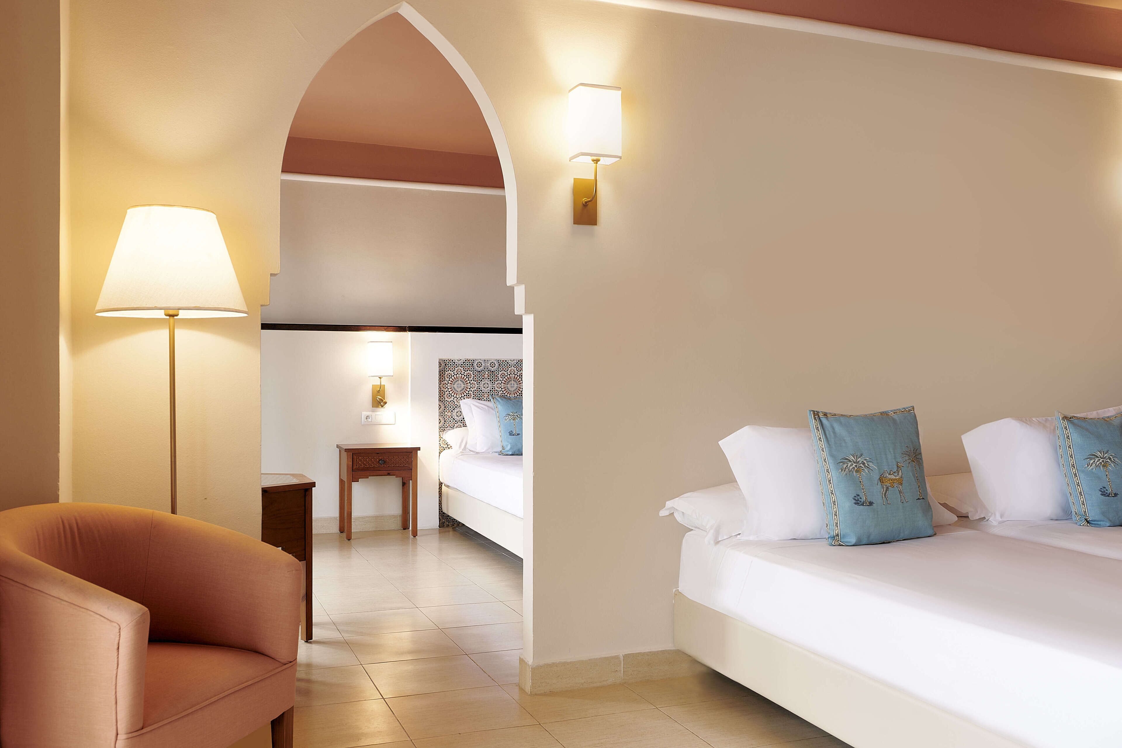 A hotel room with a sofa, a lamp, a bed with decorative pillows, and a small table with a lamp.