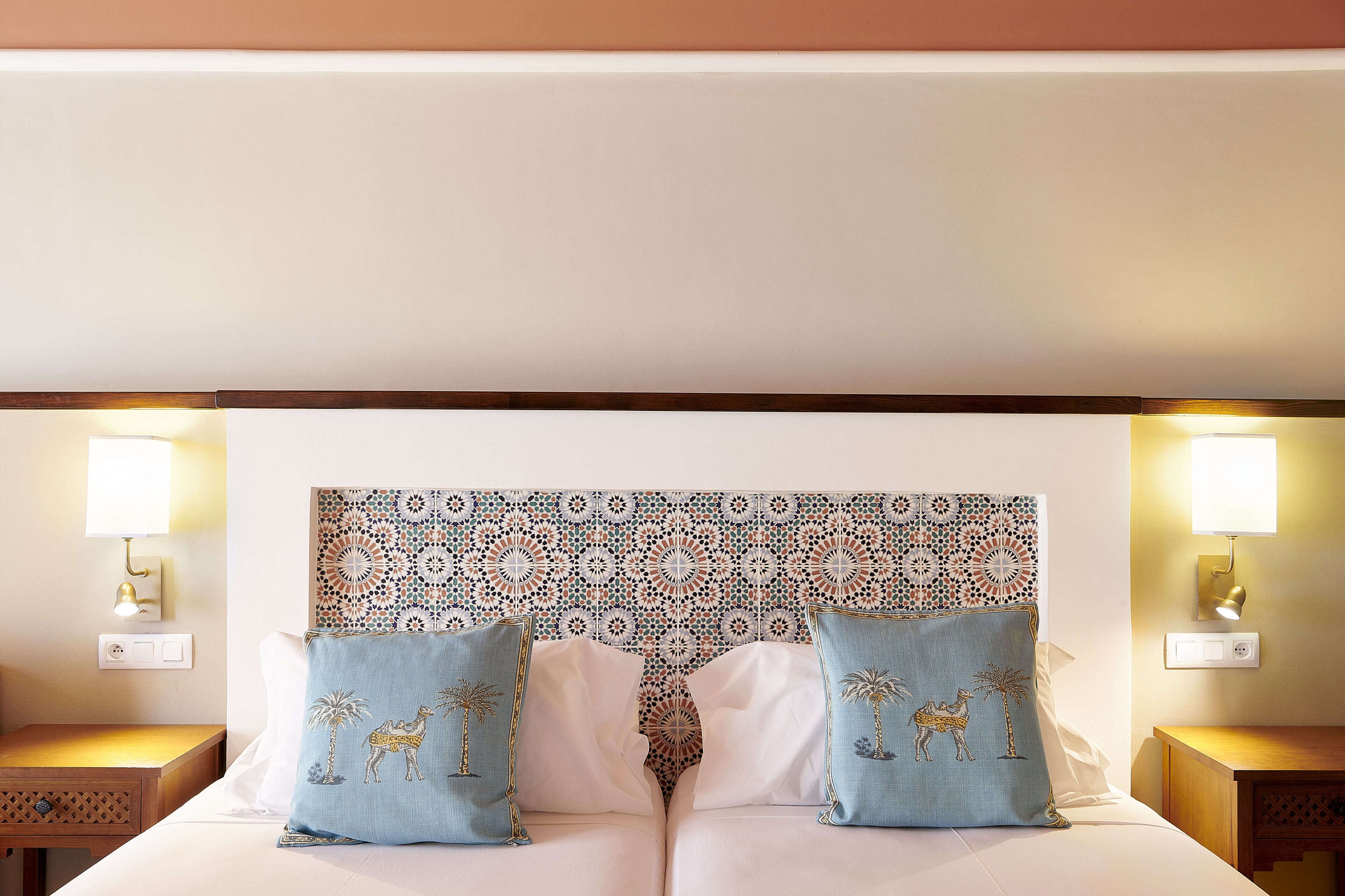 Een hotelkamer met een gestreept hoofdeinde, twee bedlampen en decoratieve kussens.
