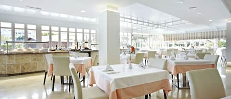 A spacious dining area with multiple tables and chairs, large windows offering views of the outdoors, and a well-lit interior.