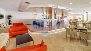 A modern hotel lobby with a bar area, seating arrangements, and a clean, polished floor. - Grupotel Port d'Alcudia (Alcúdia)