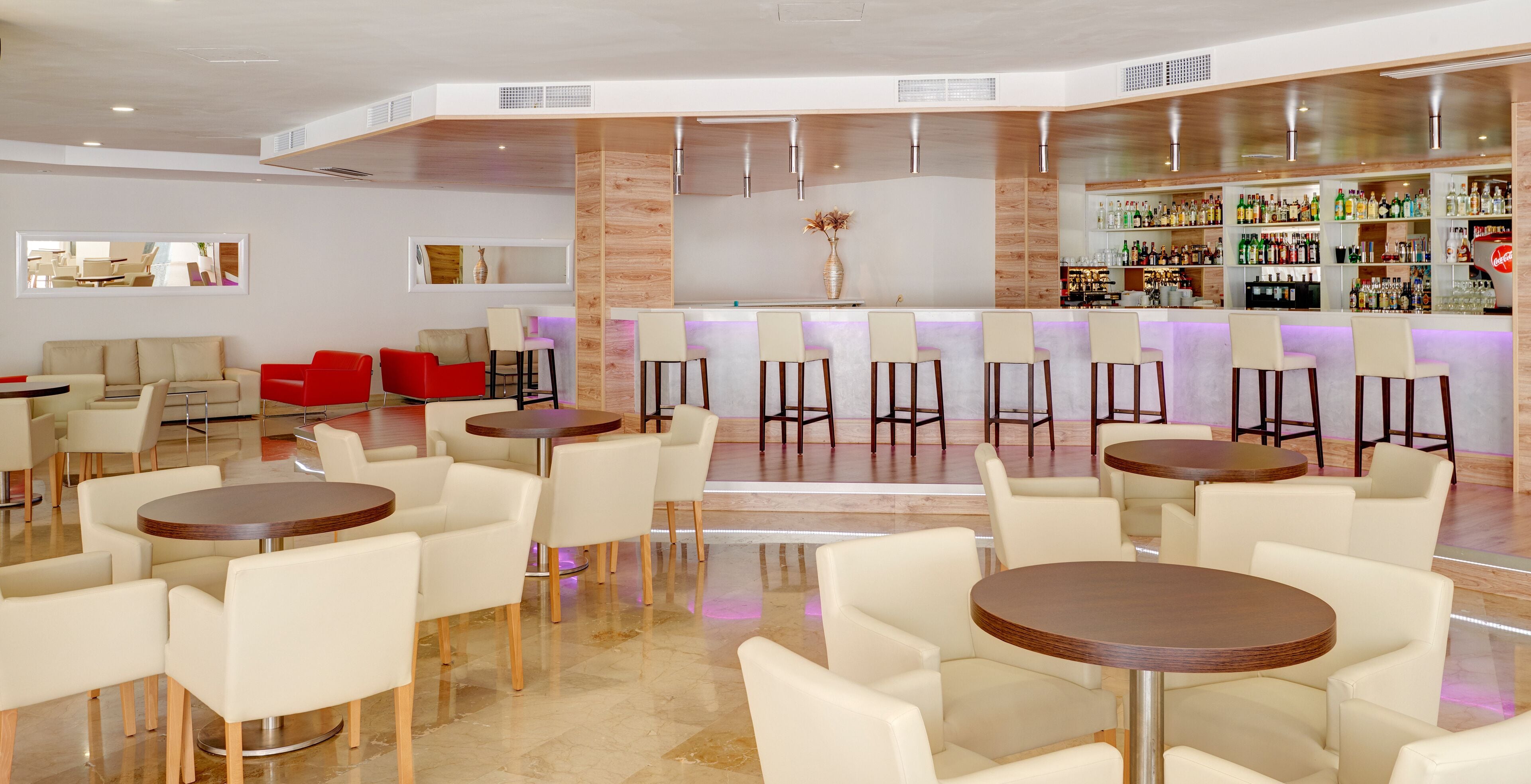 A modern bar area with multiple seating options, including round tables and bar stools, and a well-stocked liquor display.