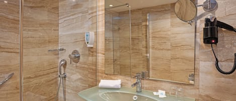 Une salle de bain moderne dotée d’un lavabo en verre, d’une douchette à main, d’un sèche-cheveux et d’un grand miroir.
