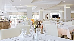 A spacious restaurant with multiple tables, each set with white tablecloths, silverware, and clear glassware. - Grupotel Port d'Alcudia (Alcúdia)