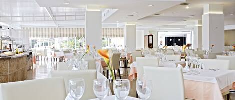 A spacious restaurant with multiple tables, each set with white tablecloths, silverware, and clear glassware.