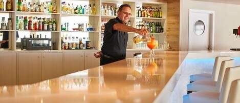 A bar area with a bartender preparing a drink. Shelves with various bottles are visible in the background.
