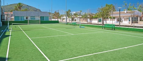 Cancha de tenis con una red, bancos verdes y cielo despejado.