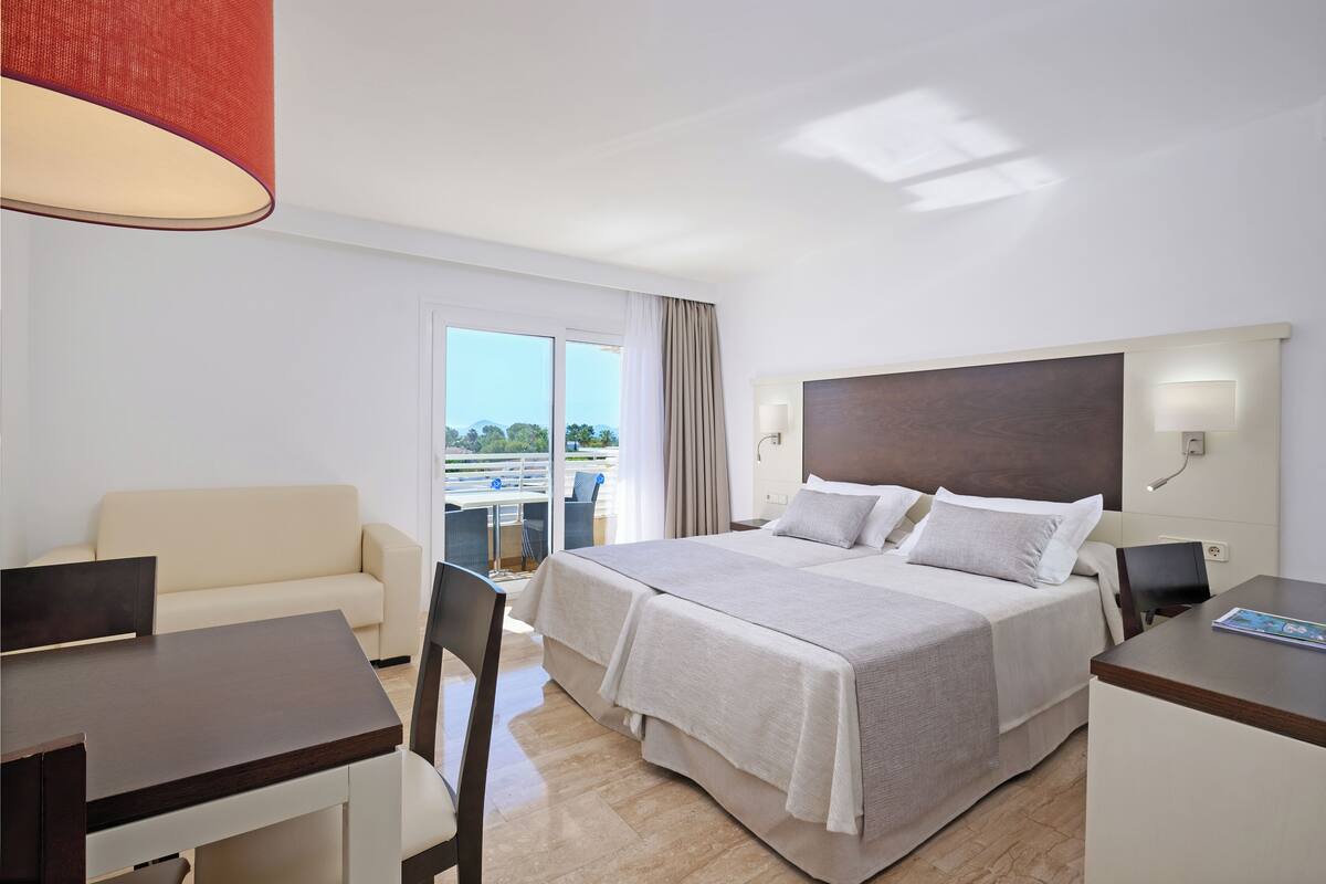 A hotel room with a bed, a desk, a chair, a sofa, and a balcony with a view.