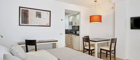 A modern, well-lit room with a bed, a desk, and a dining table.