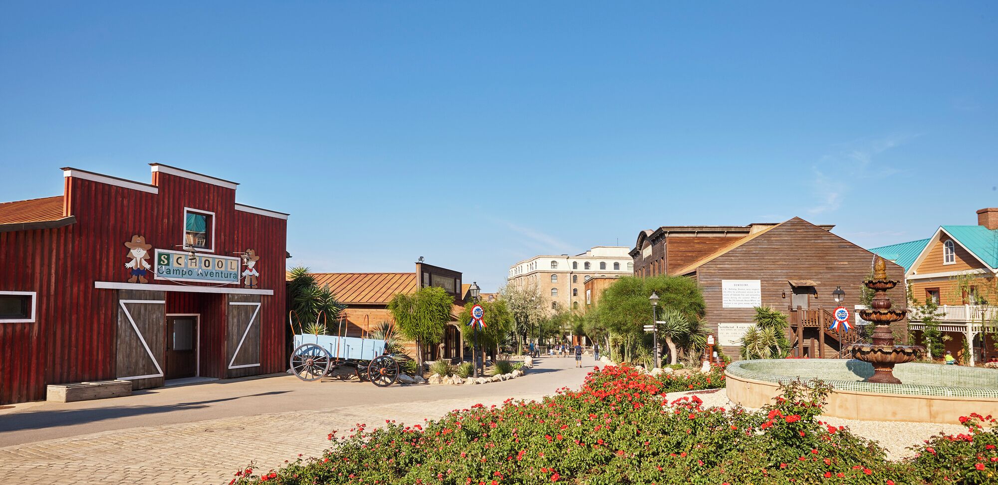 A historic town square with vintage buildings, a fountain, and a sign for 'SCAMPOOL Campo Aventura'.