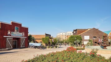 A historic town square with vintage buildings, a fountain, and a sign for 'SCAMPOOL Campo Aventura'.