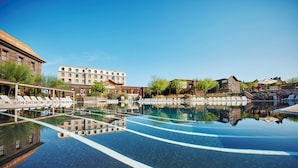 Une piscine avec des chaises longues, un bâtiment doté de nombreuses fenêtres et une structure en bois.