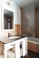 Un baño moderno con un tocador blanco, un espejo grande y una zona de ducha separada.