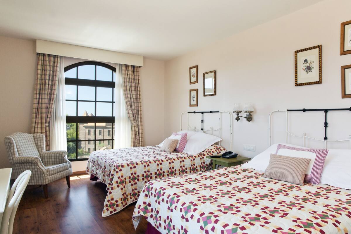 Una habitación con dos camas, una silla y un ventanal con cortinas.