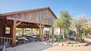 Un bâtiment rustique en bois, doté de tables et de bancs à l’extérieur, et entouré de cactus et de plantes désertiques.