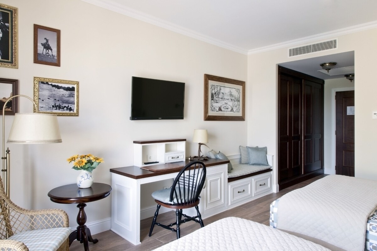 Une chambre d’hôtel avec un lit, un bureau et une chaise, une télévision et des tableaux encadrés au mur.