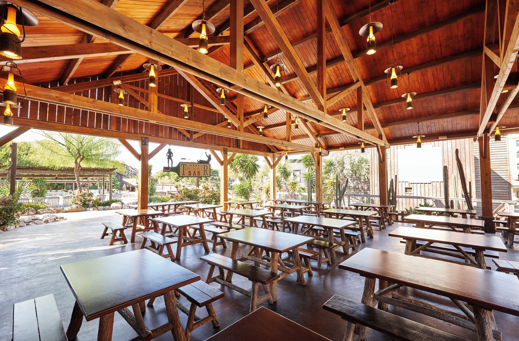An outdoor dining area with wooden tables and benches, a covered roof, and hanging lights.